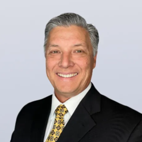 Picture of Kevin Yamano smiling with a black blazer with white dress shirt and a yellow and black patterned tie