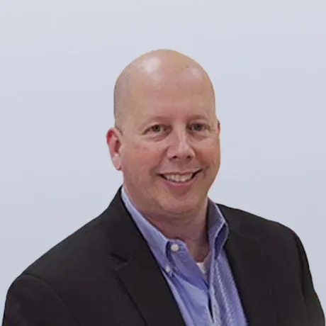 Picture of Mark Zahar smiling with a black blazer with a medium blue collard shirt open at the neck