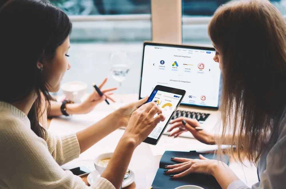 Two people looking at TapClicks interface on a laptop and iPad