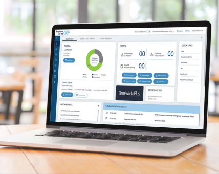 Laptop on a wooden table displaying a payroll software dashboard screen in a bright room.