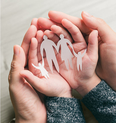 Two hands hold paper cutouts of a family, symbolizing protection and care.