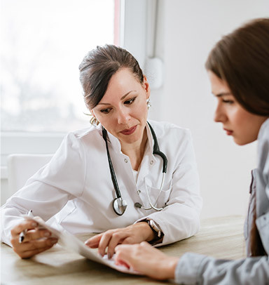 A doctor with a stethoscope discusses paperwork with a patient at a desk.