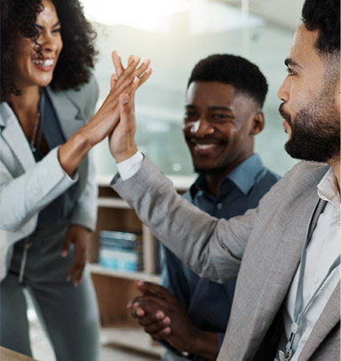 Three colleagues in suits share a high five and smile together in an office setting.