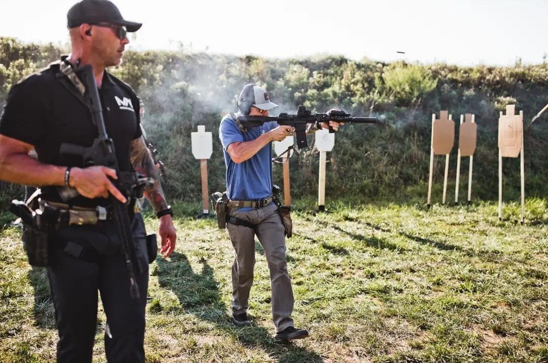 two people practicing shooting at paper targets in an outdoor firing range