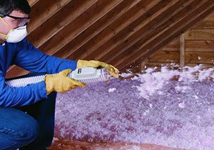 man wearing a mask and yellow gloves sprays insulation