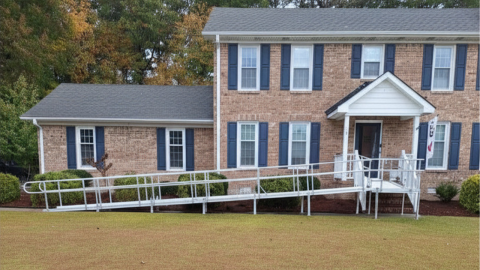 A brick house with a long metal wheelchair ramp leading up to the front entrance.