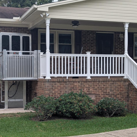 A wheelchair lift is installed beside the porch of a brick house with white railings.