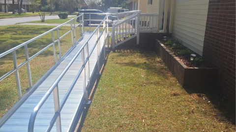 A metal wheelchair ramp leads up to the porch of a house on a sunny day.