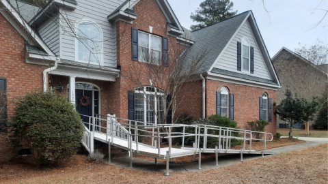A large brick house with a metal wheelchair ramp leading to the front door.
