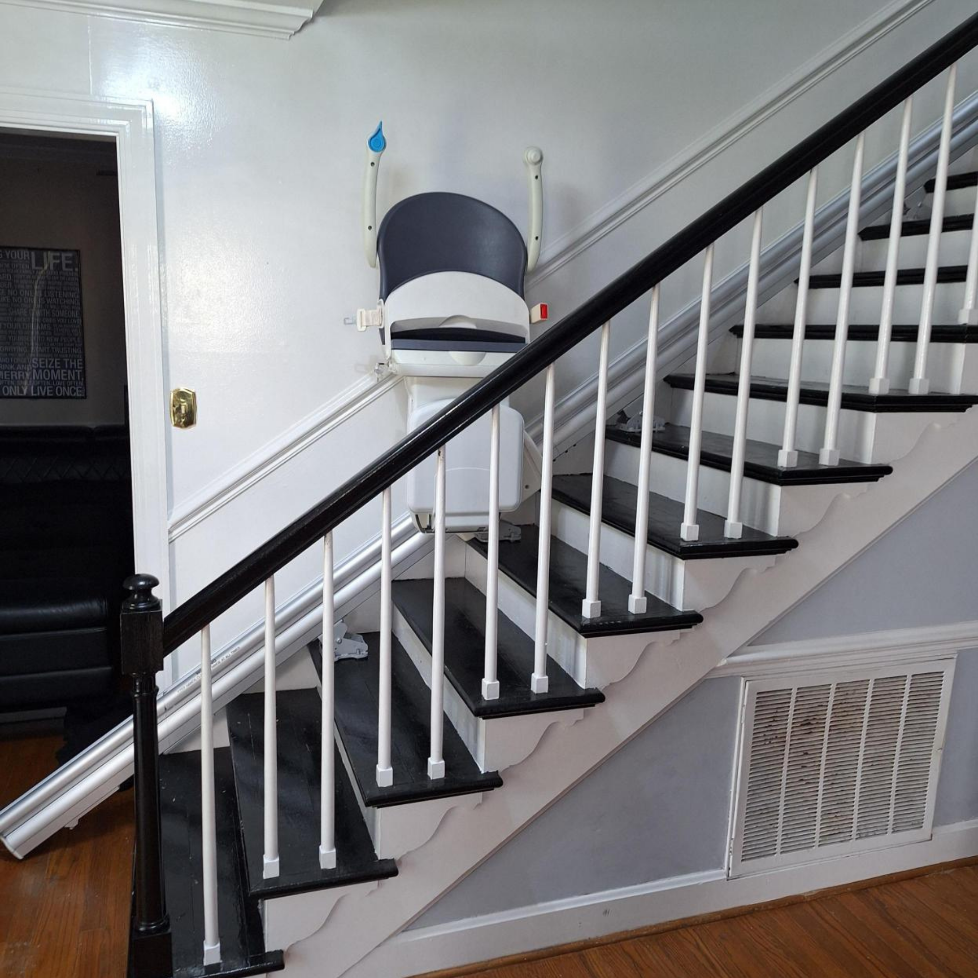 A stairlift chair is installed along a black and white staircase in a house.