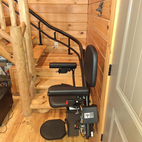 A curved stairlift is installed beside wooden stairs in a log cabin-style interior.