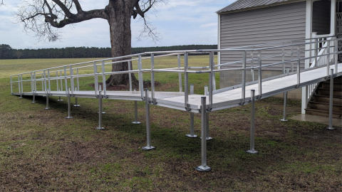 An outdoor metal wheelchair ramp leads up to the entrance of a building beside a tree.