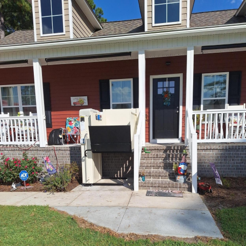 A tipped-over refrigerator sits in front of the steps of a red house with a front porch.