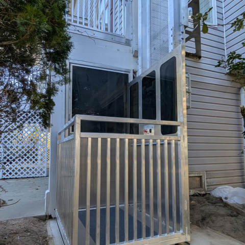 A silver wheelchair lift is installed outside a building near an entrance with a black door.