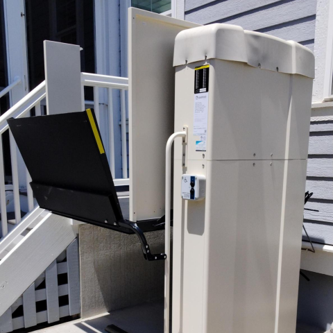 Outdoor wheelchair lift installed next to stairs leading up to a porch with a railing.