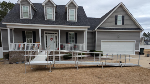 A gray house with a front porch and a metal wheelchair ramp leading to the entrance.