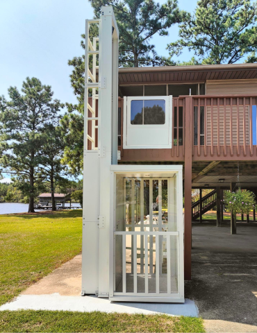 Outdoor residential elevator installed next to a raised deck, with trees and a lake in the background.