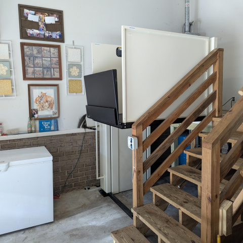 A platform lift beside wooden stairs in a garage, with pet photos and frames on the wall.