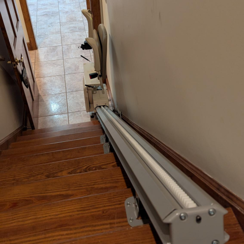 A stairlift installed on a wooden staircase next to a beige wall in a home setting.