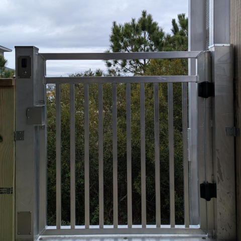 A metal gate with vertical bars is mounted on a balcony, overlooking trees and a cloudy sky.