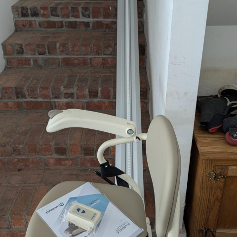 A stair lift chair at the bottom of brick stairs with instruction manuals on its seat.