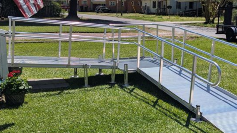 A metal wheelchair ramp with railings is installed over grass in a residential yard.