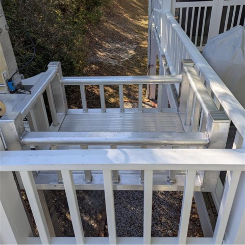 A small metal wheelchair lift platform attached to a porch, with railings and a gate.