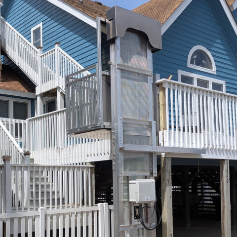 Outdoor residential elevator lift attached to a blue house with white railings and multiple decks.
