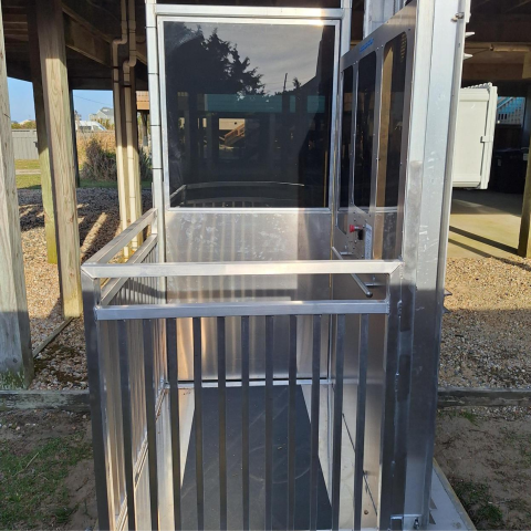 A metal outdoor wheelchair lift with railings stands beside a raised wooden structure.