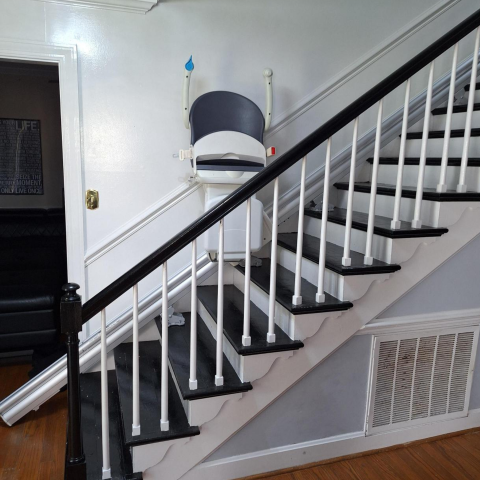 A stairlift is installed along the side of a black and white staircase in a house.