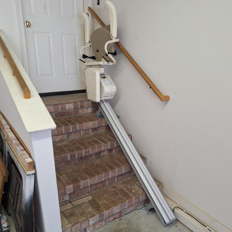 A stair lift is installed on a brick staircase in a residential garage or entryway.