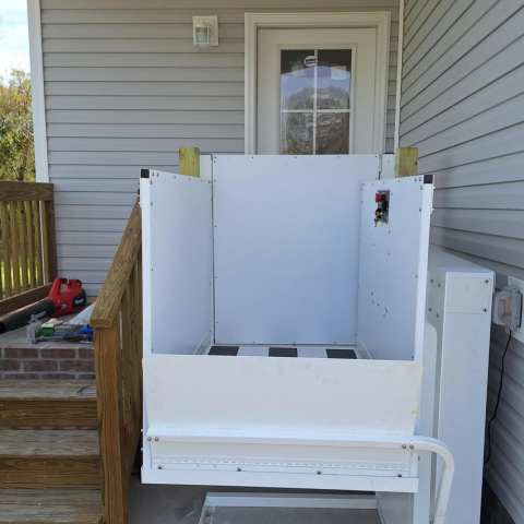 Outdoor wheelchair lift installed next to porch stairs leading up to a door of a house.