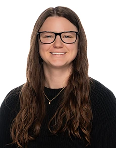 Smiling woman with long brown hair, glasses, and a black sweater on a white background.
