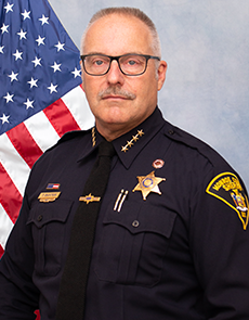 sheriff todd k baxter stands in front of an american flag
