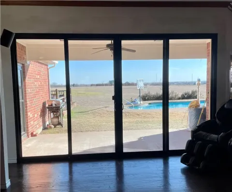 view through glass doors of a backyard with a pool, basketball hoop, and open field