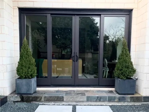 black framed glass patio doors with two potted evergreen trees on each side of the entryway