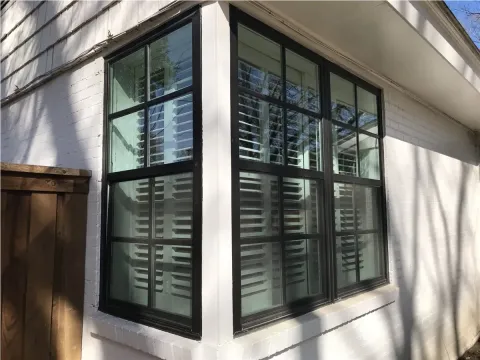 black framed bay window with white shutters on a white brick exterior wall