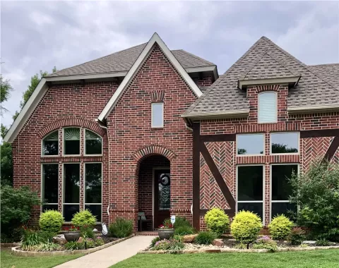 red brick house with large windows, a peaked roof, and landscaped front yard