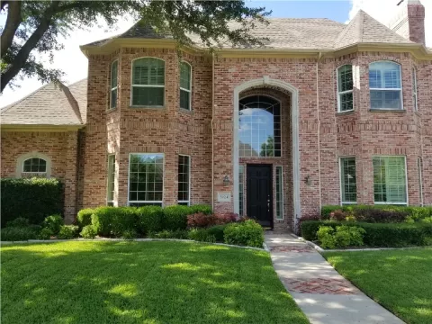 two story brick house with large windows, arched entryway, and well-kept front lawn