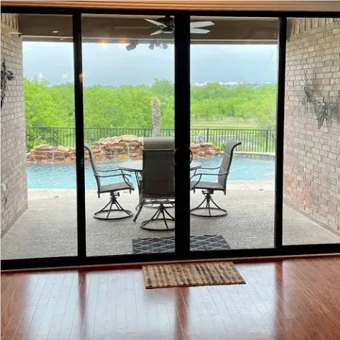 patio with chairs and table beside a pool, seen through large sliding glass doors