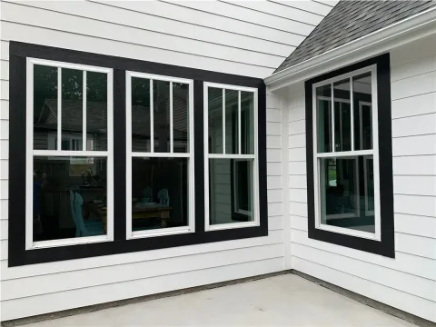 Three large black-trimmed windows on a white house with horizontal siding and a corner roof.