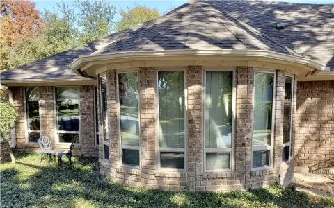 Brick house with a rounded bay window section and tall windows, with trees and shrubbery outside.