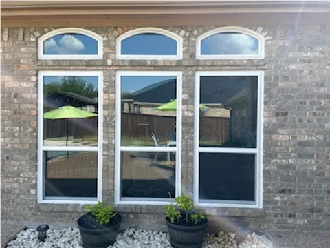 Three large windows on a brick wall reflect a patio with green umbrellas and outdoor chairs.