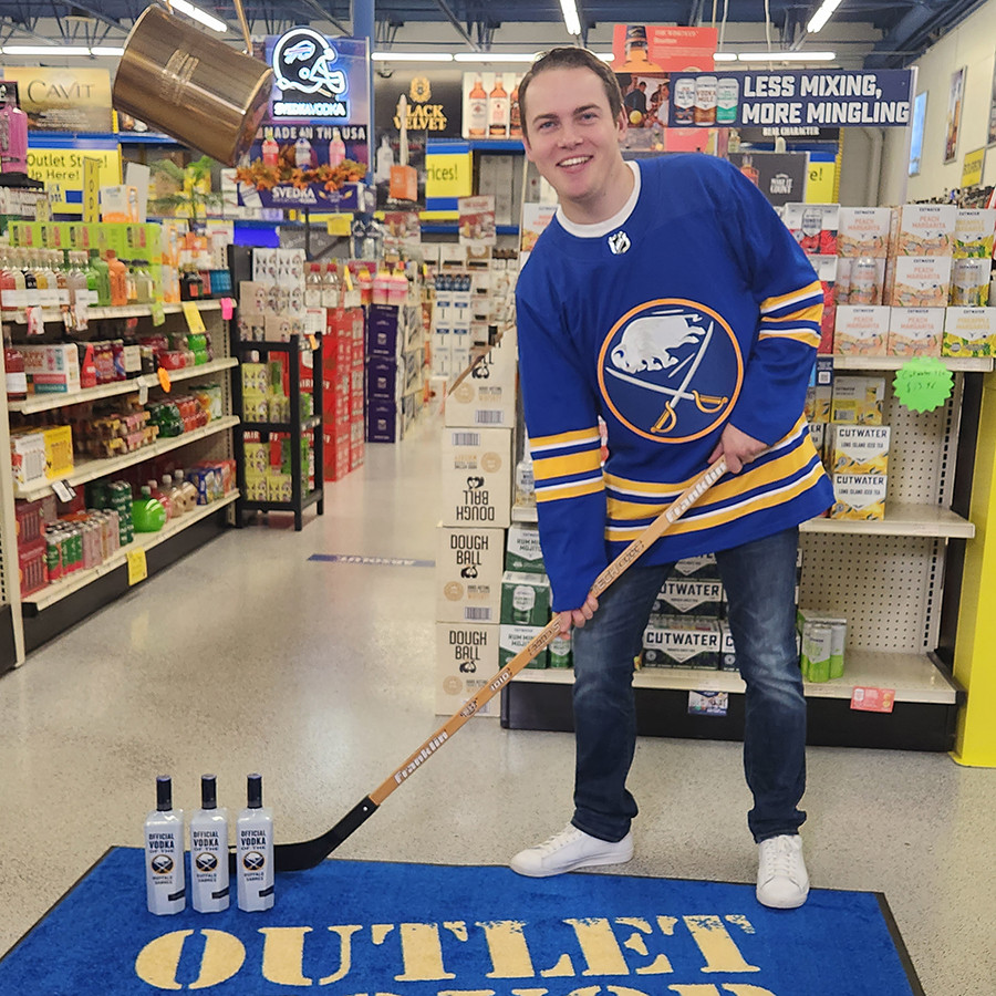 young man in hockey jersey posing with a hockey stick near bottles in liquor store