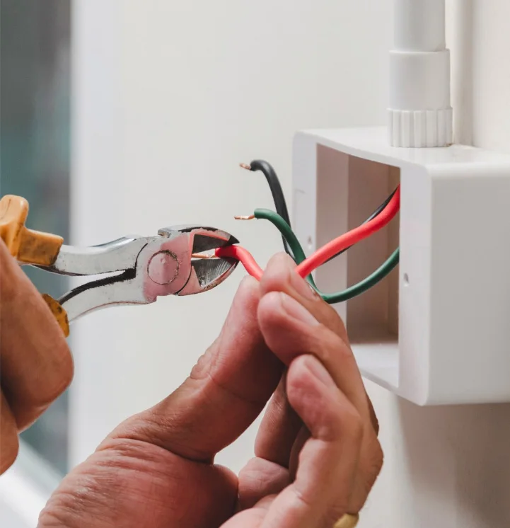 A person repairs pipes under a white sink; tools and cans are on the floor nearby.