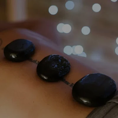 Three smooth black stones placed on a persons back during a hot stone massage, lights in background.