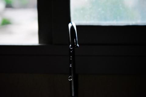 A faucet dripping water in front of a window with natural light coming through.