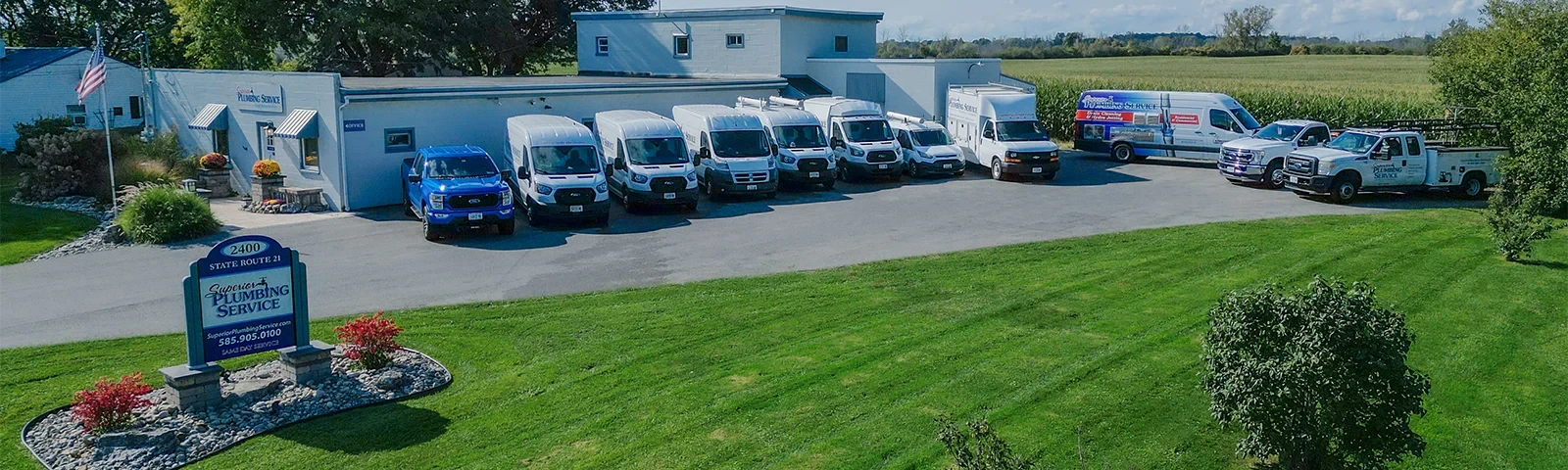row of service vehicles parked outside a building with superior plumbing service sign on lawn