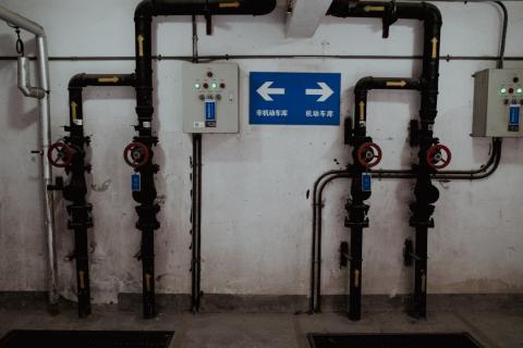 Black pipes and control panels on a wall, with a blue sign showing two white arrows.
