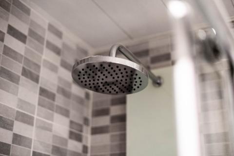 Close-up of a round metal showerhead attached to a tiled wall in a bathroom.